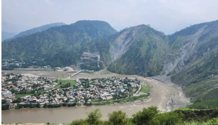 A scenic aerial view of Muzaffarabad city with the Neelum and Jhelum rivers meeting, surrounded by lush green mountains.