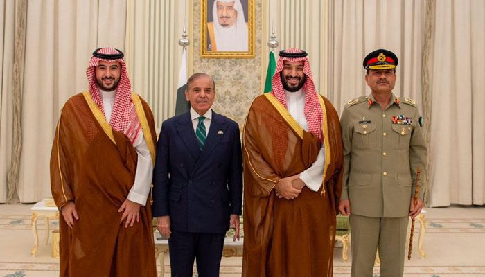 Flags of Pakistan and Saudi Arabia side-by-side on a document signing table.