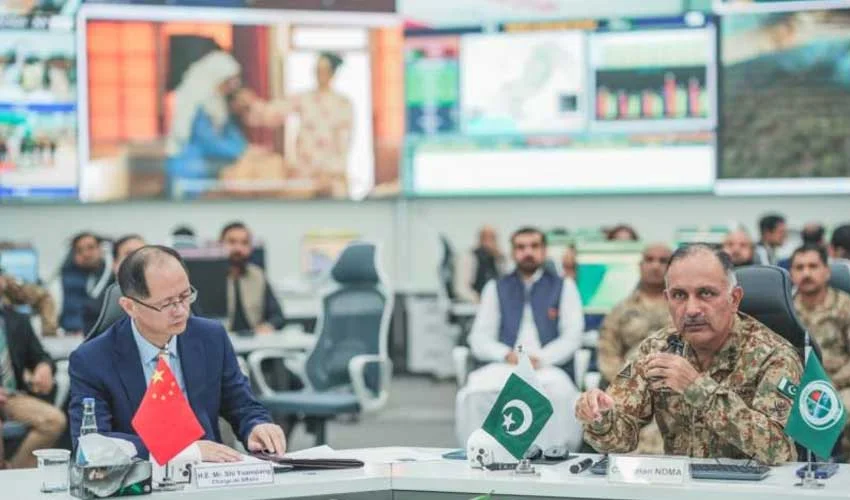Chinese and Pakistani officials discussing flood relief efforts over a map in an operations room.